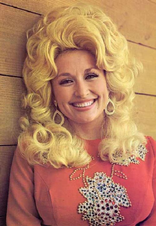 dolly parton smiling for the camera with curly hairs and lovely red dress 